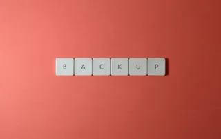 Free Close-up of keyboard keys spelling 'BACKUP' placed on a coral-colored surface. Stock Photo