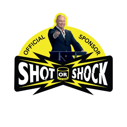 Man in a suit at a podium giving a thumbs-up, in front of a black-and-yellow 'SHOT OR SHOCK' sponsor logo with lightning bolts and 'OFFICIAL SPONSOR' text