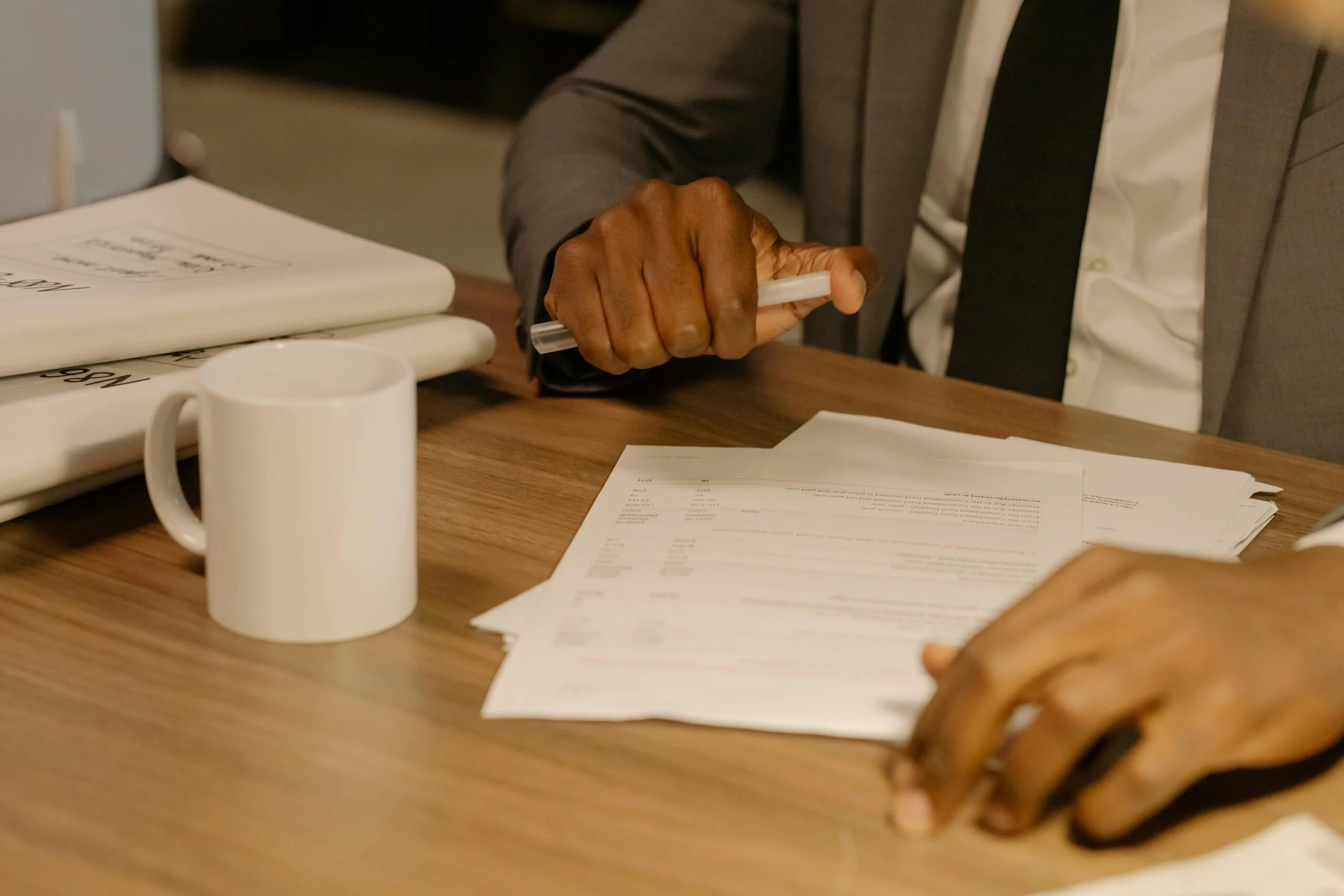 Free Close-up of a businessman holding and reviewing documents on a wooden desk. Stock Photo